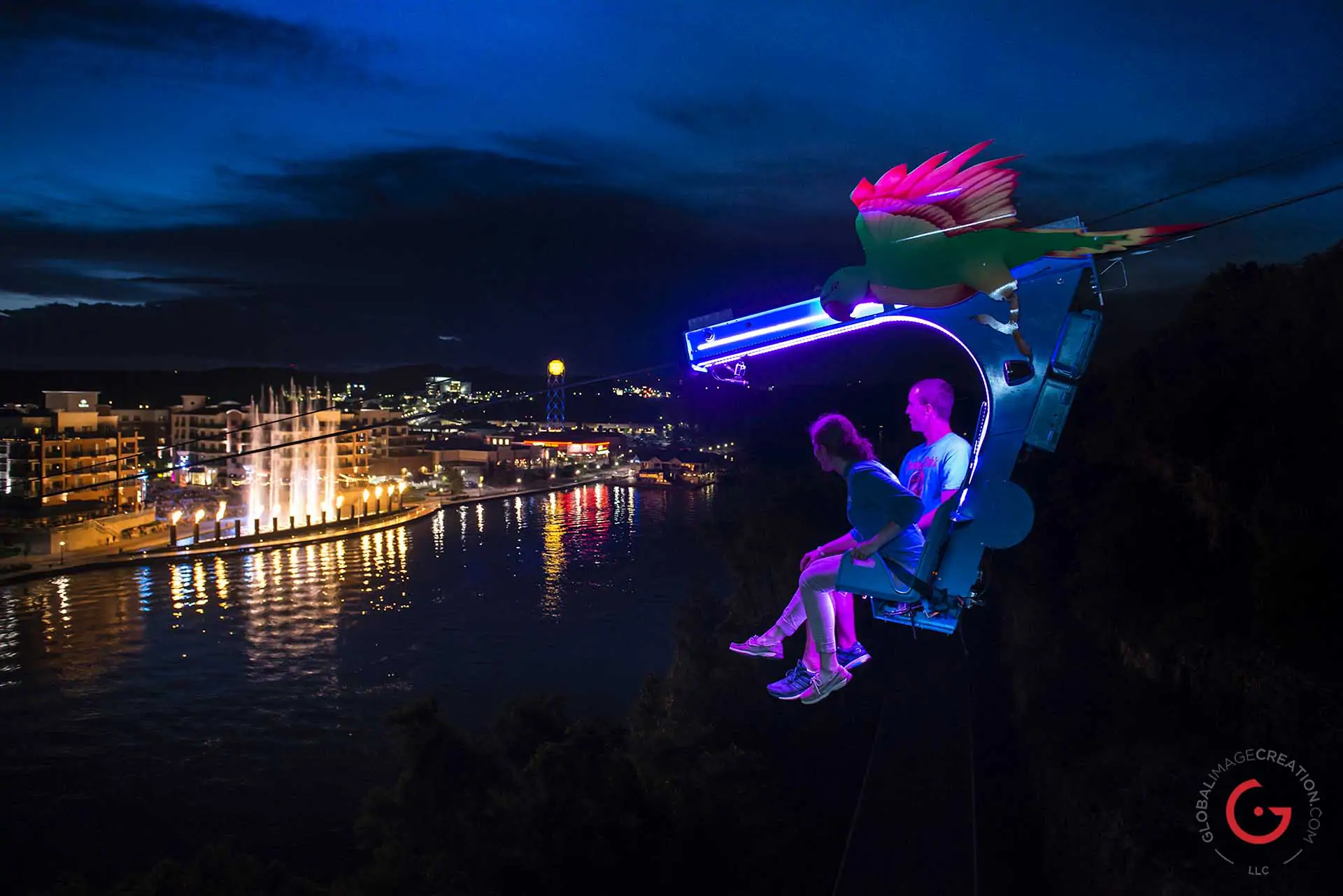 Couple rides the zip line at the Branson Landing at night while the fountain show plays in the background - Advertising photographers in Branson Missouri, Branson Missouri photography